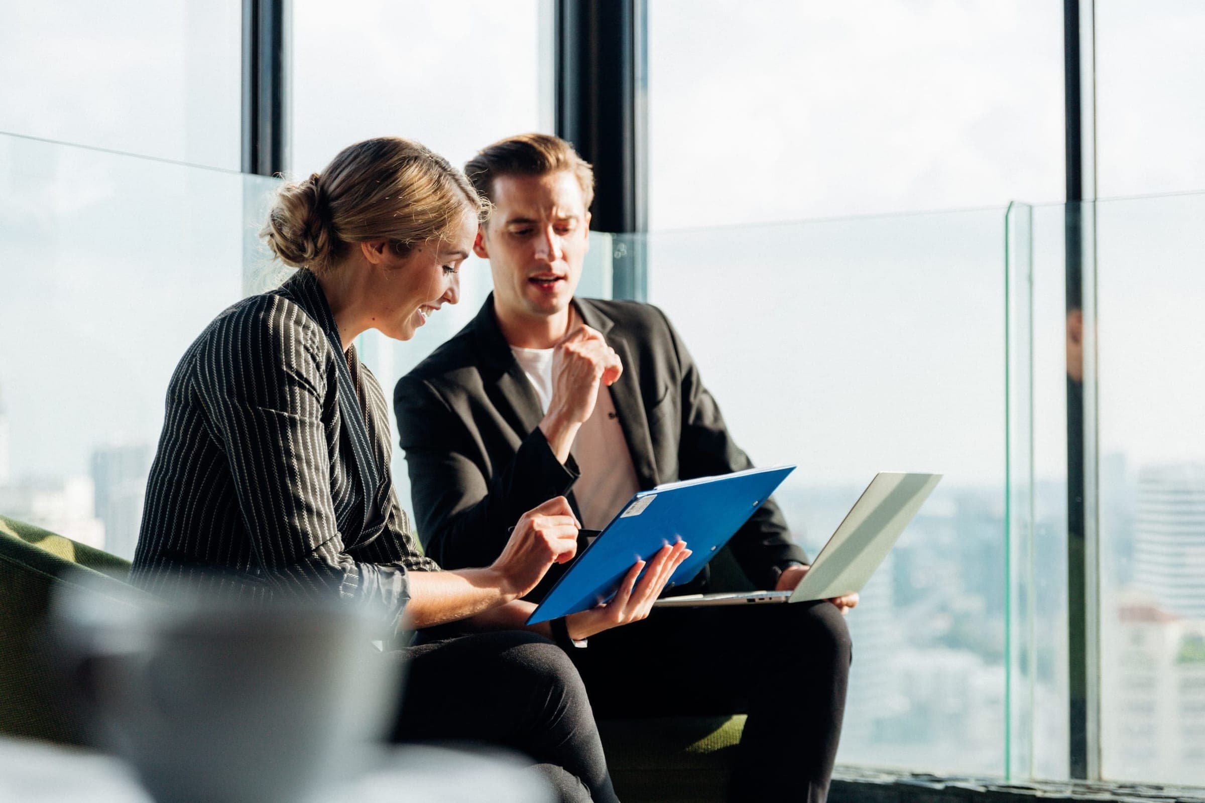 Two colleagues reviewing a document together in an office overlooking the city