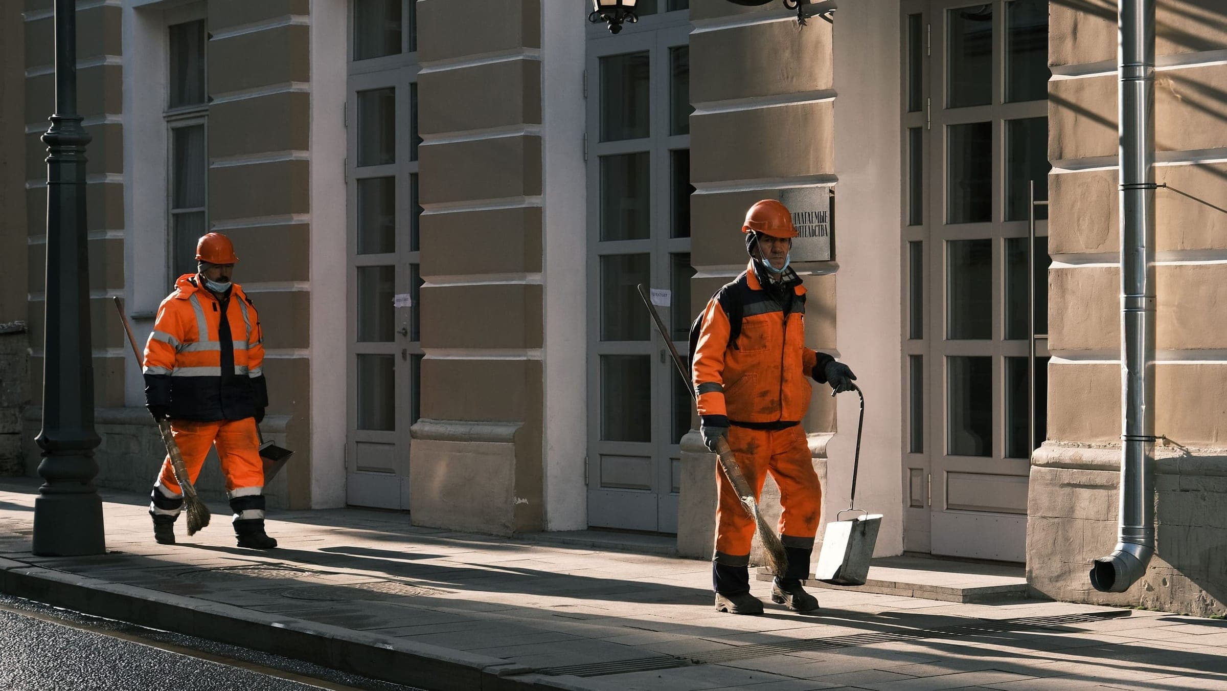 Two field technicians in high-visibility jackets walking past a building
